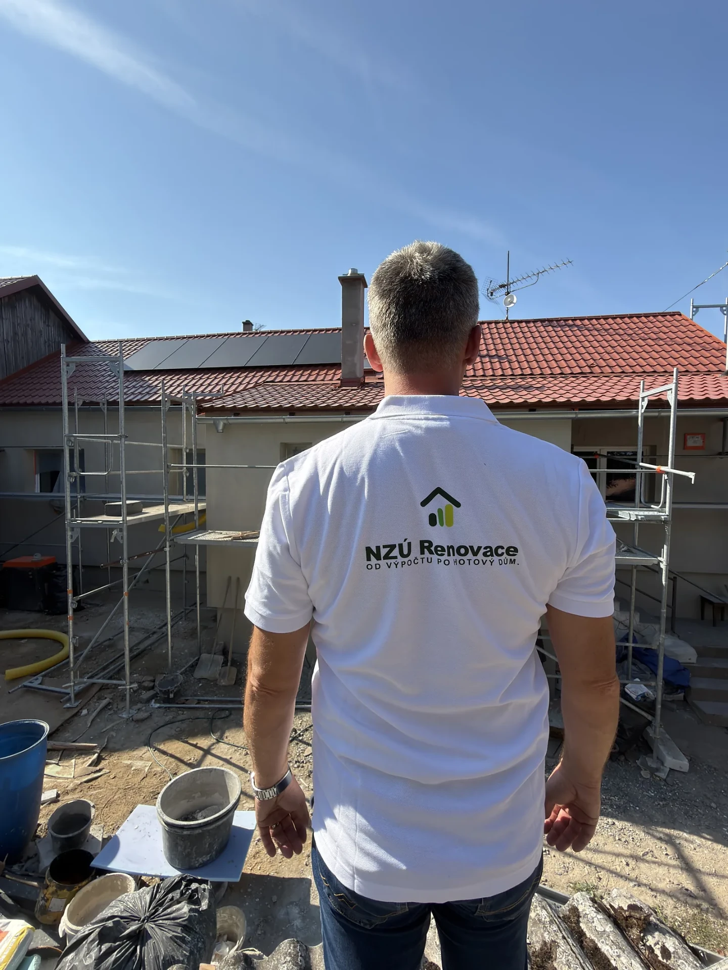 Člen týmu NZÚ Renovace stojí u domu v lešení